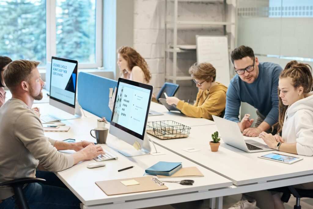 Emprego na TIVIT para Executivas de Vendas e UX/UI Team collaboration in a modern office setting with computers and diverse employees working together.