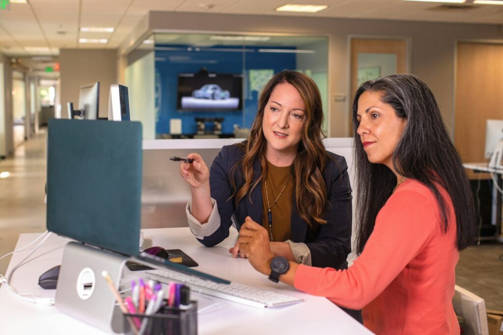 Vagas de Emprego para Auxiliar Administrativo two women sitting at a table looking at a computer screen