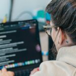 Boom de cursos no Brasil: Como escolher formações que realmente geram empregabilidade? Woman with glasses coding on a laptop computer.