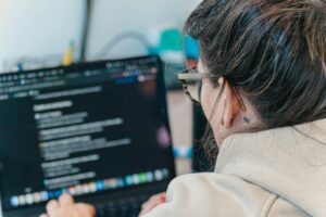 Boom de cursos no Brasil: Como escolher formações que realmente geram empregabilidade? Woman with glasses coding on a laptop computer.