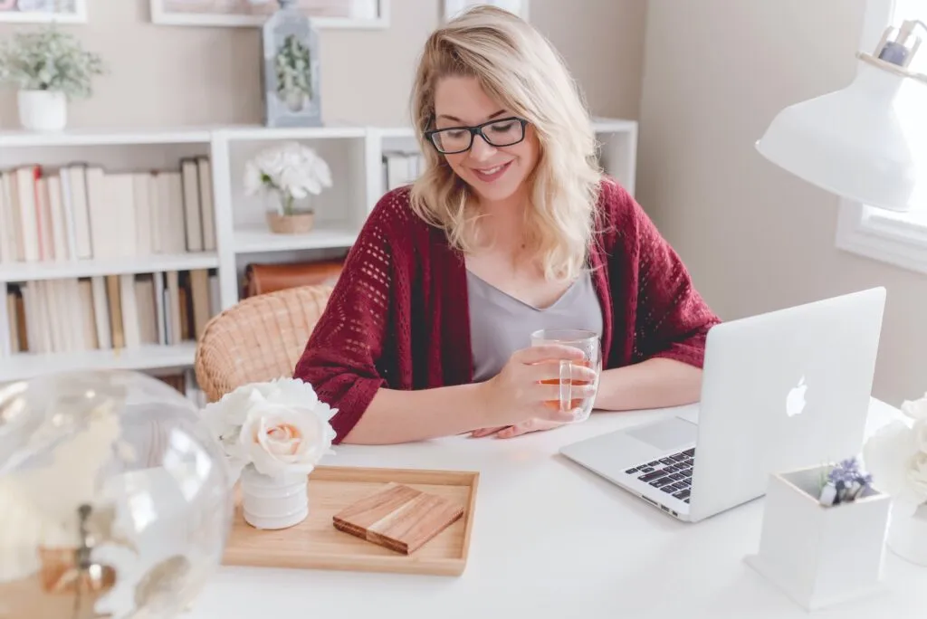 DBServices woman smiling holding glass mug sitting beside table with MacBook