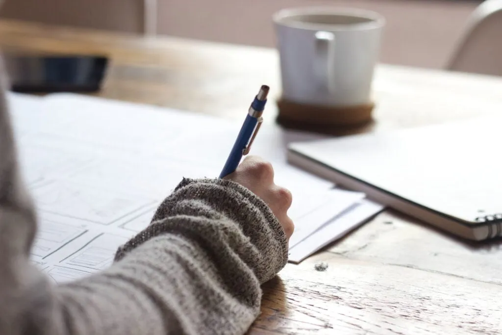 A Crise Educacional no Brasil Photo by Unseen Studio person writing on brown wooden table near white ceramic mug